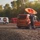 A photo of someone taking a kayak off the roof of an orange Transit Connect van.